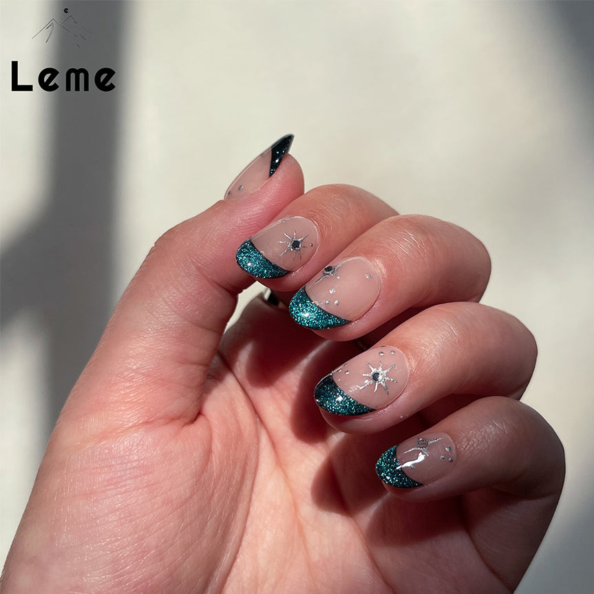 Blue Night is a reusable handmade press-on nails set by Leme. Experience the elegance of our "Blue Night" manicure featuring expertly crafted cat-eye French tips on a subtle nude base. Each short oval-shaped nail is adorned with delicate silver stars and sparkling diamonds, creating a refined and sophisticated look. This design balances understated charm with a touch of luxury, perfect for those seeking a polished and unique style.