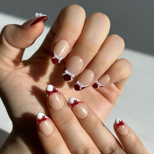 Candy Bow is a reusable handmade press-on nails set by Leme. Elevate your manicure with Candy Bow, a sophisticated press-on nail set featuring a nude base and multiple refined shapes available. Each tip showcases hand-applied French detailing in crisp red and white, crowned with delicate red and white 3D bow accents for a polished, editorial finish. Crafted from premium materials, these nails deliver salon-quality results with effortless application. Perfect for adding a touch of refined elegance to any occ