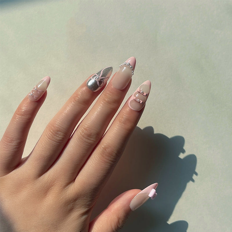 Charlotte is a reusable handmade press-on nails set by Leme. Elevate your nail game with Charlotte, a delicate ballet-inspired press-on set that captures timeless elegance. This medium almond design features a soft nude base with chic pink French tips, accented by two shimmering chrome nails for a modern touch. Tiny pearls delicately adorn select nails, while adorable pink bows grace each thumb—a whimsical detail that brings the entire look together. Perfect for those who love a refined, romantic aesthetic