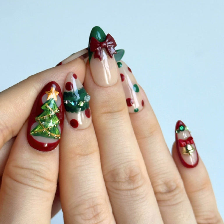 Christmas Song is a reusable handmade press-on nails set by Leme. Celebrate the season with Christmas Song, a sophisticated press-on nail set featuring medium almond-shaped nails in festive green and red. Each nail showcases meticulous artistry: delicate green cat-eye designs adorn the thumbs with a Christmas tree motif and golden cat-eye stars on top. The index and ring fingers feature gem-embellished Christmas wreaths. Dimensional 3D bows on French tips on the middle fingers, and ornate golden bells on th