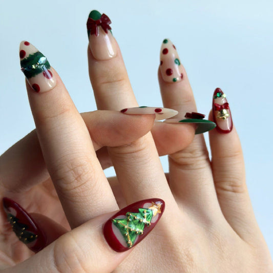 Christmas Song is a reusable handmade press-on nails set by Leme. Celebrate the season with Christmas Song, a sophisticated press-on nail set featuring medium almond-shaped nails in festive green and red. Each nail showcases meticulous artistry: delicate green cat-eye designs adorn the thumbs with a Christmas tree motif and golden cat-eye stars on top. The index and ring fingers feature gem-embellished Christmas wreaths. Dimensional 3D bows on French tips on the middle fingers, and ornate golden bells on th