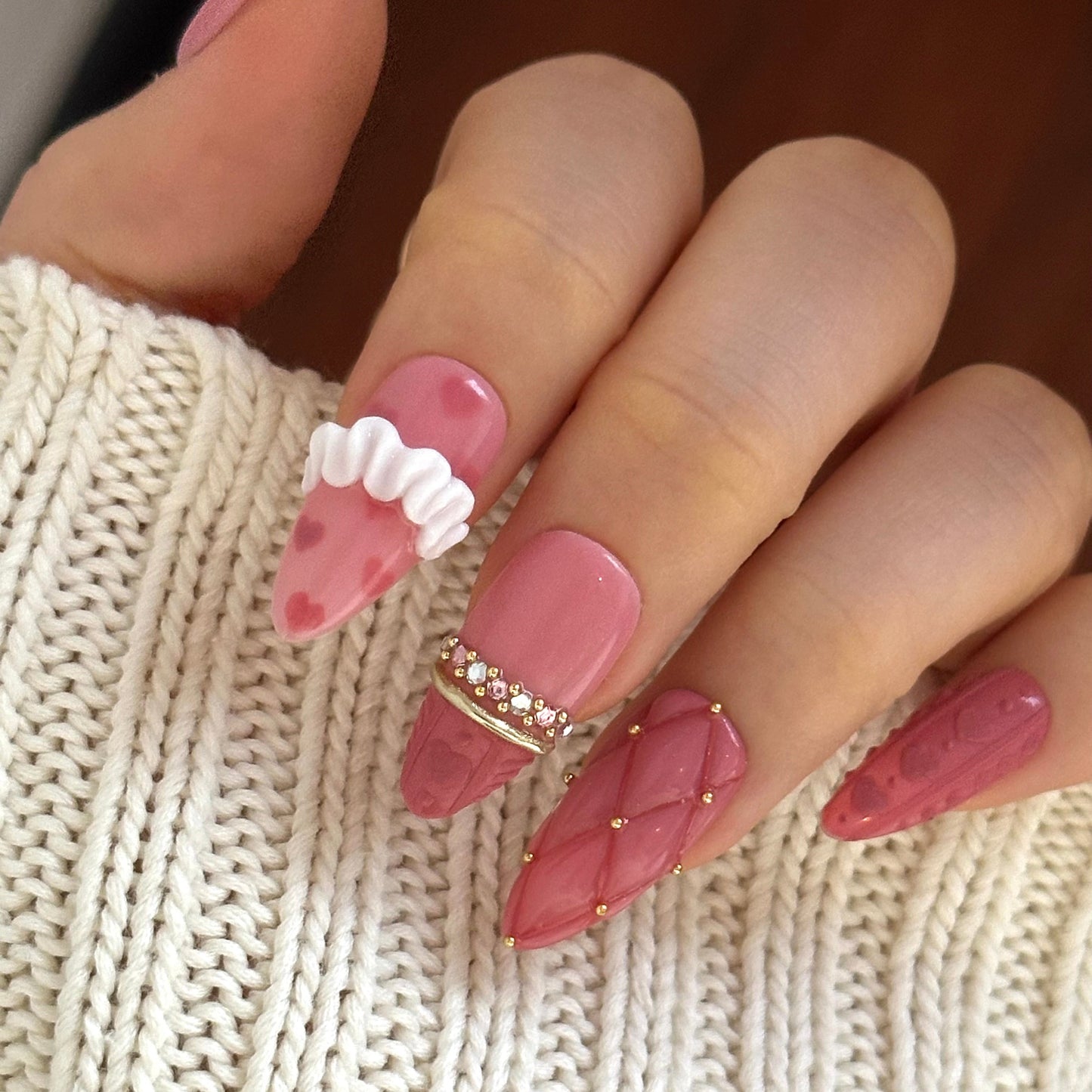 Gold Promise is a reusable handmade press-on nails set by Leme. Discover Gold Promise, an exquisite nail collection that captures timeless elegance through meticulous craftsmanship. These medium almond-shaped nails feature a romantic pink base paired with classic French tips adorned in a soft sweater texture for subtle sophistication. The design showcases premium 3D embellishments complemented by strategically placed gems and gold chrome accents that form delicate ring-like details across the nail surface.