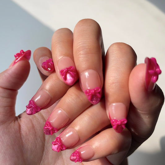 Sassy Diva is a reusable handmade press-on nails set by Leme. Elevate your manicure with the Sassy Diva nails, featuring a short almond shape and classic French tips enhanced by a vibrant hot pink cat-eye effect. Each nail is adorned with a delicate pink bow tie over a nude base, combining elegance with a playful edge. Crafted with high-quality materials, these nails offer durability and a flawless finish for a confident, expert look.