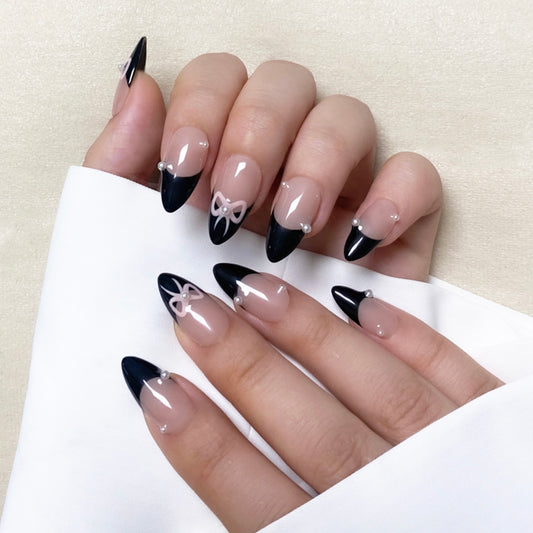 Tie Me is a reusable handmade press-on nails set by Leme. Elevate your nail style with "Tie Me," featuring expertly crafted almond-shaped nails and intricate 3D designs. These high-quality nails showcase a chic nude base accented by elegant black French tips and a delicate pink bow tie design, combining sophistication with a playful touch. Perfect for those seeking a refined yet unique manicure look.