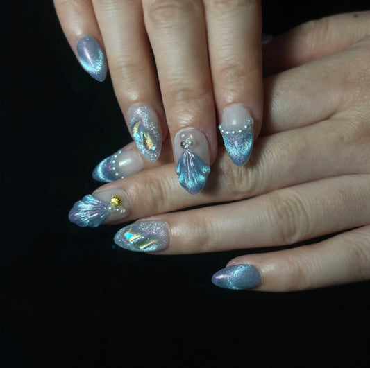 Treasure Beneath is a reusable handmade press-on nails set by Leme. Experience the elegance of "Treasure Beneath" nails, featuring expertly crafted short almond-shaped tips with a sophisticated blue cat-eye effect. These high-quality 3D nails showcase delicate water-inspired designs on a pristine white base, accented with lustrous pearls for a refined, dimensional look. Perfect for those seeking a subtle yet striking manicure that combines artistry with durability.