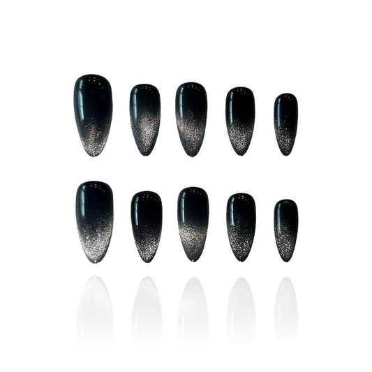 Black Stardust is a reusable handmade press-on nails set by Leme. Transform your nail aesthetic with these exquisite black stardust nails, expertly designed with a medium almond shape that elongates the fingers and creates an elegant silhouette. The deep black base is beautifully complemented by shimmering silver accents that sparkle with every movement, delivering a luxurious finish that captures light magnificently. Crafted from premium materials, these high-quality nails offer superior durability.