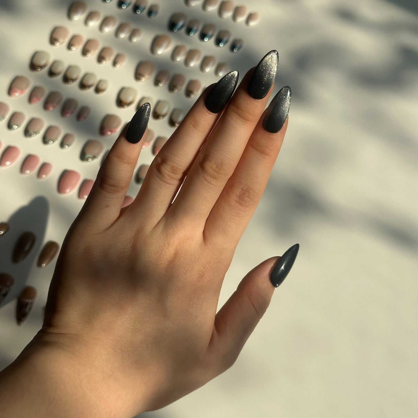 Black Stardust is a reusable handmade press-on nails set by Leme. Transform your nail aesthetic with these exquisite black stardust nails, expertly designed with a medium almond shape that elongates the fingers and creates an elegant silhouette. The deep black base is beautifully complemented by shimmering silver accents that sparkle with every movement, delivering a luxurious finish that captures light magnificently. Crafted from premium materials, these high-quality nails offer superior durability and a f