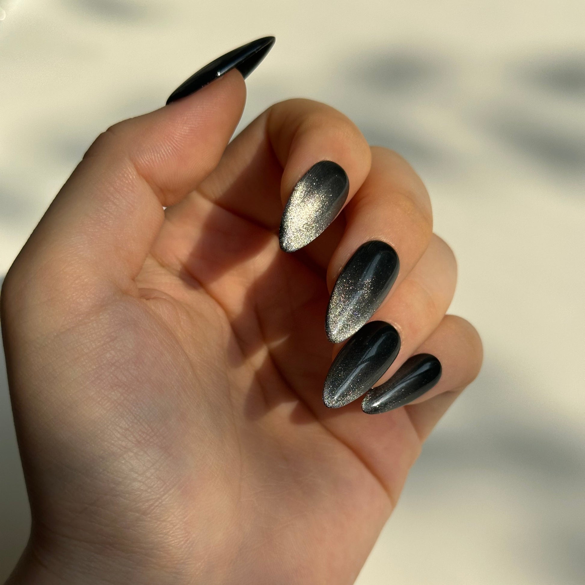 Black Stardust is a reusable handmade press-on nails set by Leme. Transform your nail aesthetic with these exquisite black stardust nails, expertly designed with a medium almond shape that elongates the fingers and creates an elegant silhouette. The deep black base is beautifully complemented by shimmering silver accents that sparkle with every movement, delivering a luxurious finish that captures light magnificently. Crafted from premium materials, these high-quality nails offer superior durability and a f