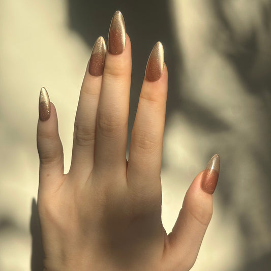 Bronze Latte is a reusable handmade press-on nails set by Leme. It delivers sophisticated elegance with a medium almond silhouette that flatters any hand shape. The rich brown base is elevated by luminous golden shimmers that catch light beautifully, creating depth and dimension. The classic cat-eye design adds a contemporary edge, making these nails perfect for both everyday wear and special occasions. Crafted with premium materials for durability and a flawless finish that lasts.