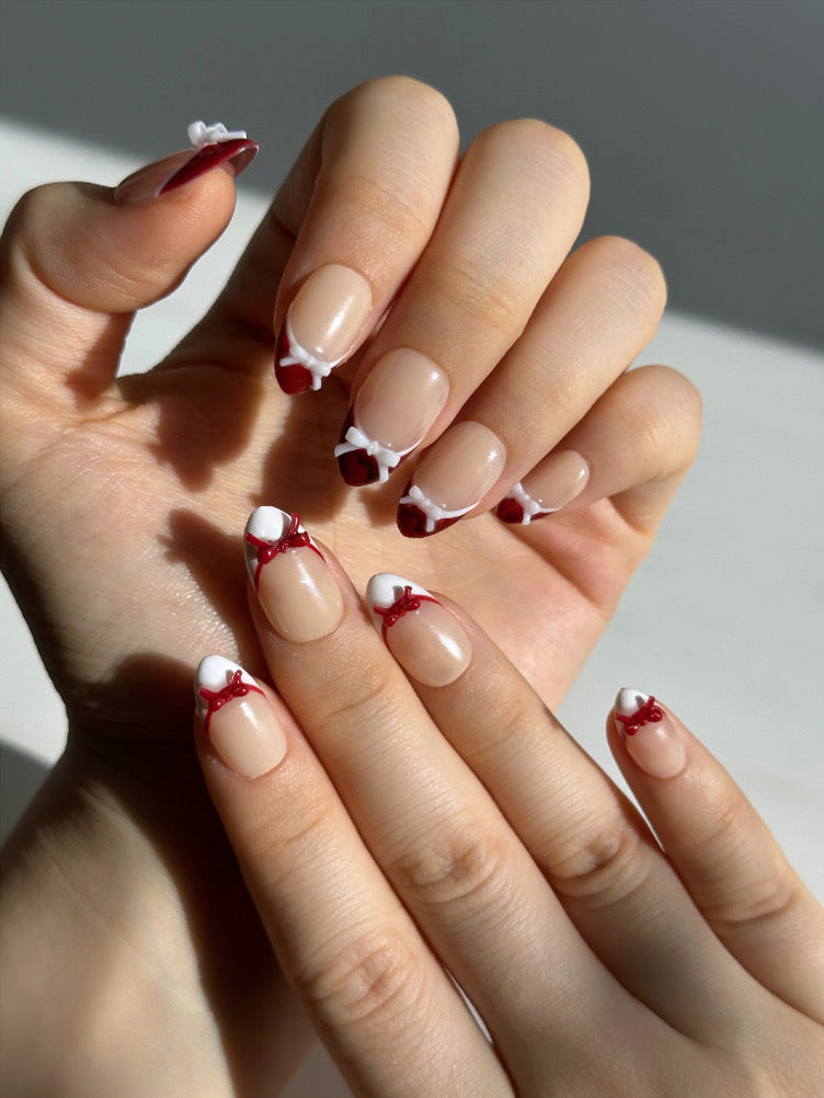 Candy Bow is a reusable handmade press-on nails set by Leme. Elevate your manicure with Candy Bow, a sophisticated press-on nail set featuring a nude base and multiple refined shapes available. Each tip showcases hand-applied French detailing in crisp red and white, crowned with delicate red and white 3D bow accents for a polished, editorial finish. Crafted from premium materials, these nails deliver salon-quality results with effortless application. Perfect for adding a touch of refined elegance to any occ