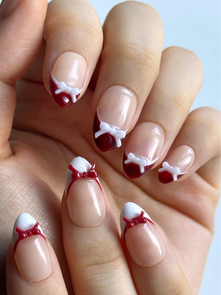 Candy Bow is a reusable handmade press-on nails set by Leme. Elevate your manicure with Candy Bow, a sophisticated press-on nail set featuring a nude base and multiple refined shapes available. Each tip showcases hand-applied French detailing in crisp red and white, crowned with delicate red and white 3D bow accents for a polished, editorial finish. Crafted from premium materials, these nails deliver salon-quality results with effortless application. Perfect for adding a touch of refined elegance to any occ