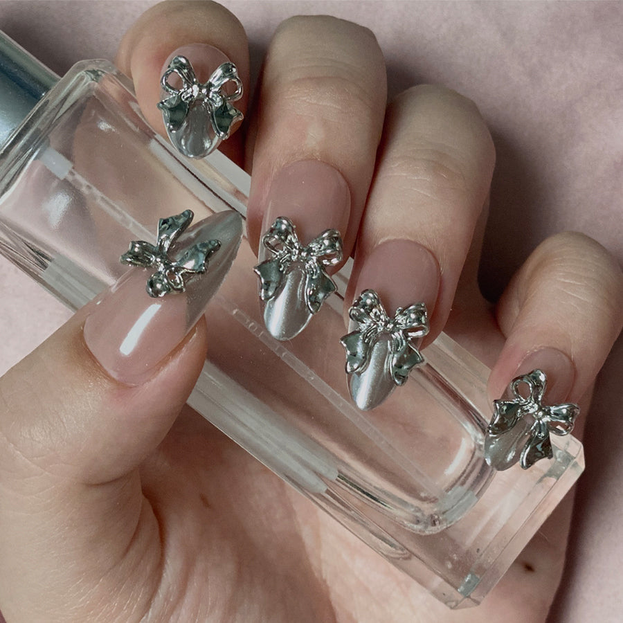 Flying Platinum is a reusable handmade press-on nails set by Leme. Elevate your nail game with Flying Platinum, a stunning set of medium almond-shaped press-on nails designed for the modern sophisticate. Each nail features a luxurious nude base paired with high-shine silver chrome French tips and intricate 3D silver bowties that catch the light beautifully. Handcrafted for a premium finish, these reusable nails deliver salon-quality results in seconds. Perfect for adding a touch of elegance to any occasion,