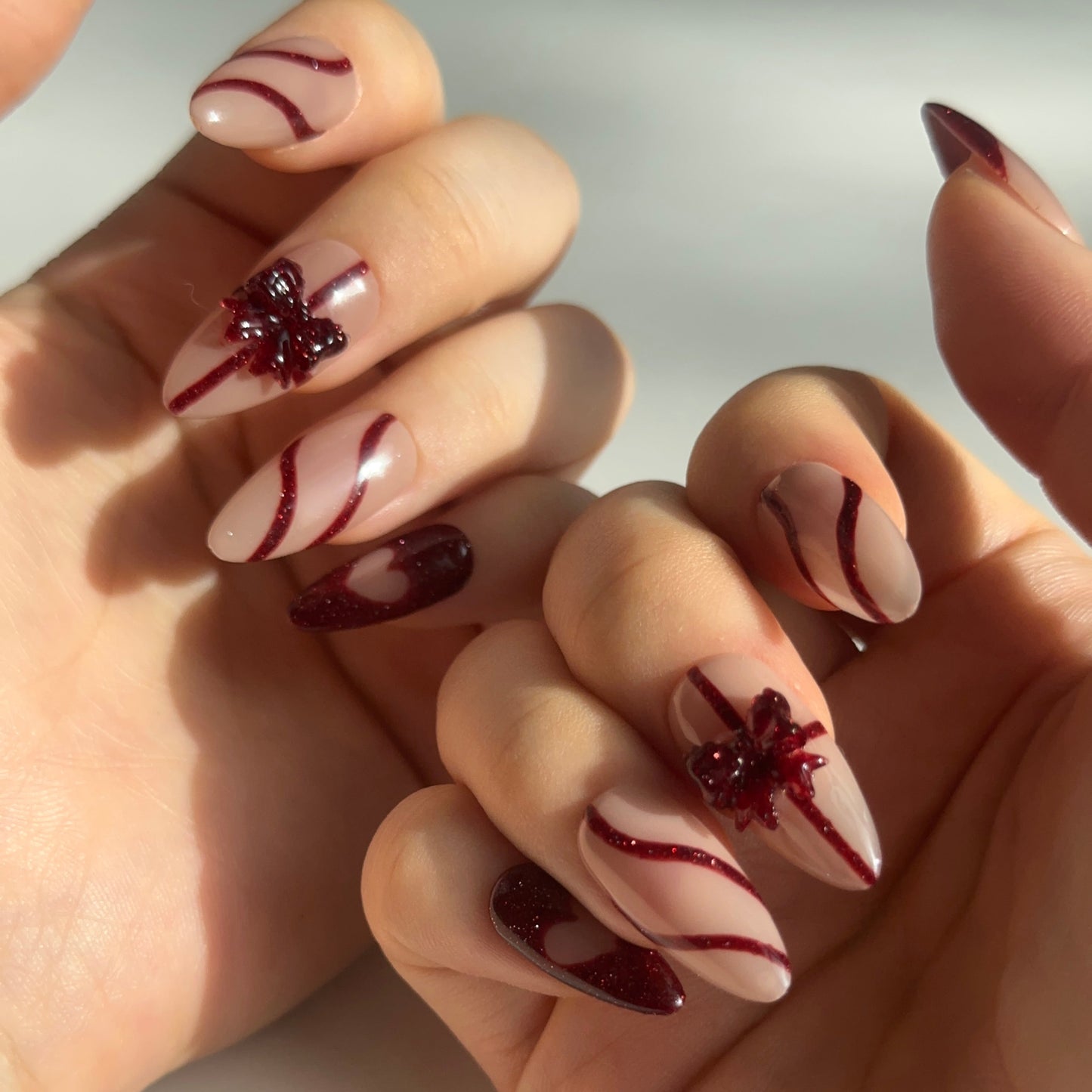 Gift Box is a reusable handmade press-on nails set by Leme. Elevate your nail game with this sophisticated press-on set featuring a medium almond shape and timeless French tip design. The nude base provides a versatile canvas, while glitter red accents add glamorous dimension. Delicate 3D bows adorning the middle fingers create a refined focal point that balances elegance with playful detail. Crafted from premium materials for a salon-quality finish, this set delivers professional results with effortless ap