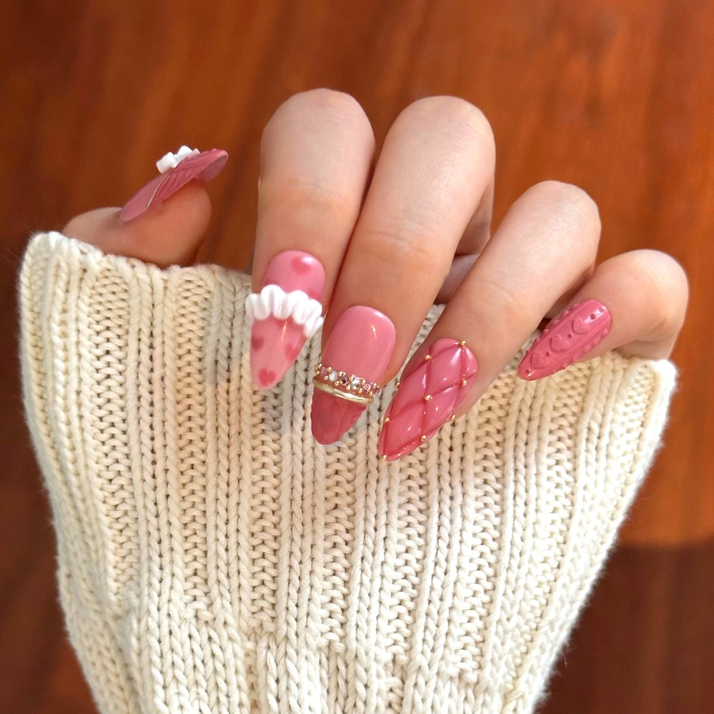Gold Promise is a reusable handmade press-on nails set by Leme. Discover Gold Promise, an exquisite nail collection that captures timeless elegance through meticulous craftsmanship. These medium almond-shaped nails feature a romantic pink base paired with classic French tips adorned in a soft sweater texture for subtle sophistication. The design showcases premium 3D embellishments complemented by strategically placed gems and gold chrome accents that form delicate ring-like details across the nail surface. 