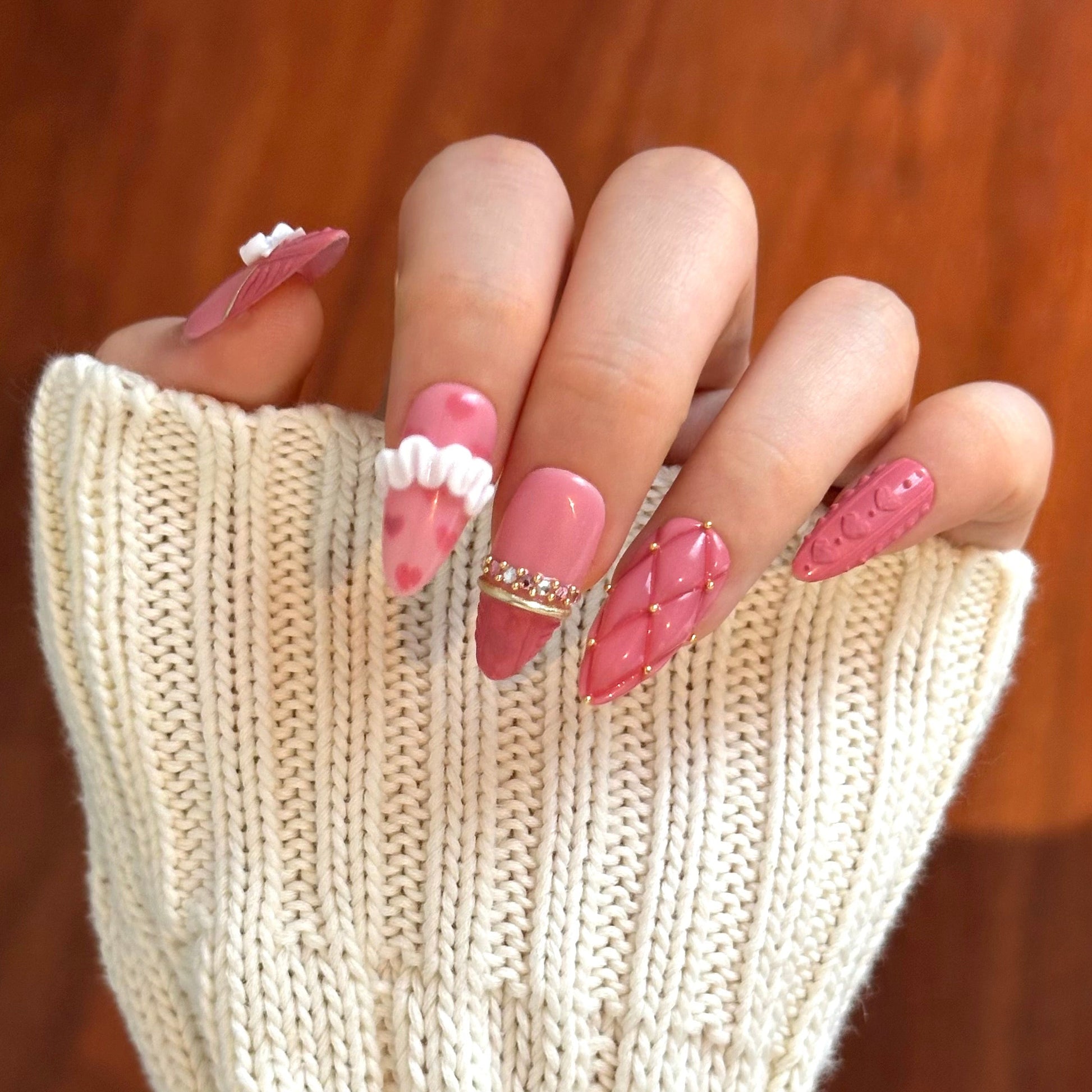 Gold Promise is a reusable handmade press-on nails set by Leme. Discover Gold Promise, an exquisite nail collection that captures timeless elegance through meticulous craftsmanship. These medium almond-shaped nails feature a romantic pink base paired with classic French tips adorned in a soft sweater texture for subtle sophistication. The design showcases premium 3D embellishments complemented by strategically placed gems and gold chrome accents that form delicate ring-like details across the nail surface. 