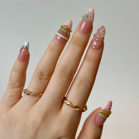 Gold Spark is a reusable handmade press-on nails set by Leme. Elevate your nail game with Gold Spark, a stunning collection of medium almond-shaped press-on nails featuring intricate French tips and playful polka dot designs. Each nail is adorned with luxurious 3D decorations, delicate gold bangles, and shimmering blue and pink diamond accents that catch the light with every gesture. Crafted from high-quality materials, these nails deliver a salon-perfect finish with a complex, eye-catching design that make