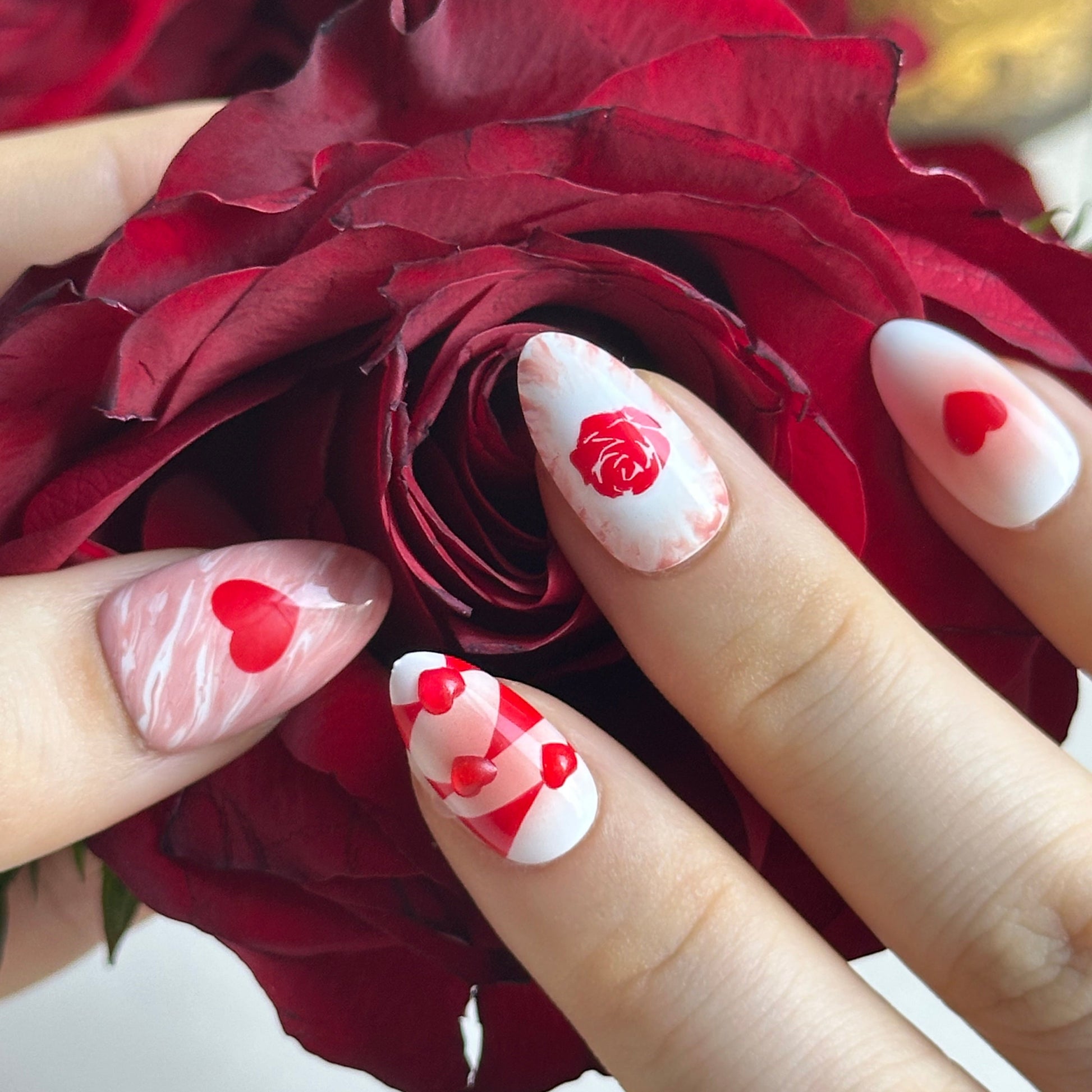 Rosy Ocean is a reusable handmade press-on nails set by Leme. Rosy Ocean captures the essence of romance with its expertly crafted design. Featuring hand-drawn rose paired with delicate 3D hearts, this short almond-shaped nail set delivers a sophisticated yet playful aesthetic. The Valentine's collection showcases a harmonious blend of white, pink, and red tones that complement any complexion. Each nail displays meticulous attention to detail, making this a standout choice for those seeking distinctive, hig