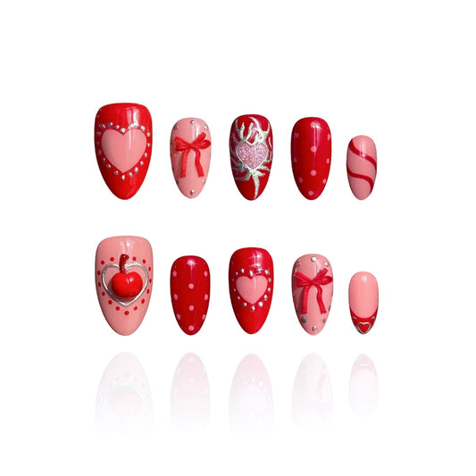 Silver Kisses is a reusable handmade press-on nails set by Leme. Elevate your Valentine's Day look with Silver Kisses, a high-quality short almond nail design from our exclusive Valentine's collection. This striking design features lustrous silver chrome accents paired with dimensional 3D cherry details, creating an eye-catching contrast. The bold palette of hot red and pink celebrates uninhibited romance and passionate self-expression. A glittering heart adorns the middle finger as the statement focal poin