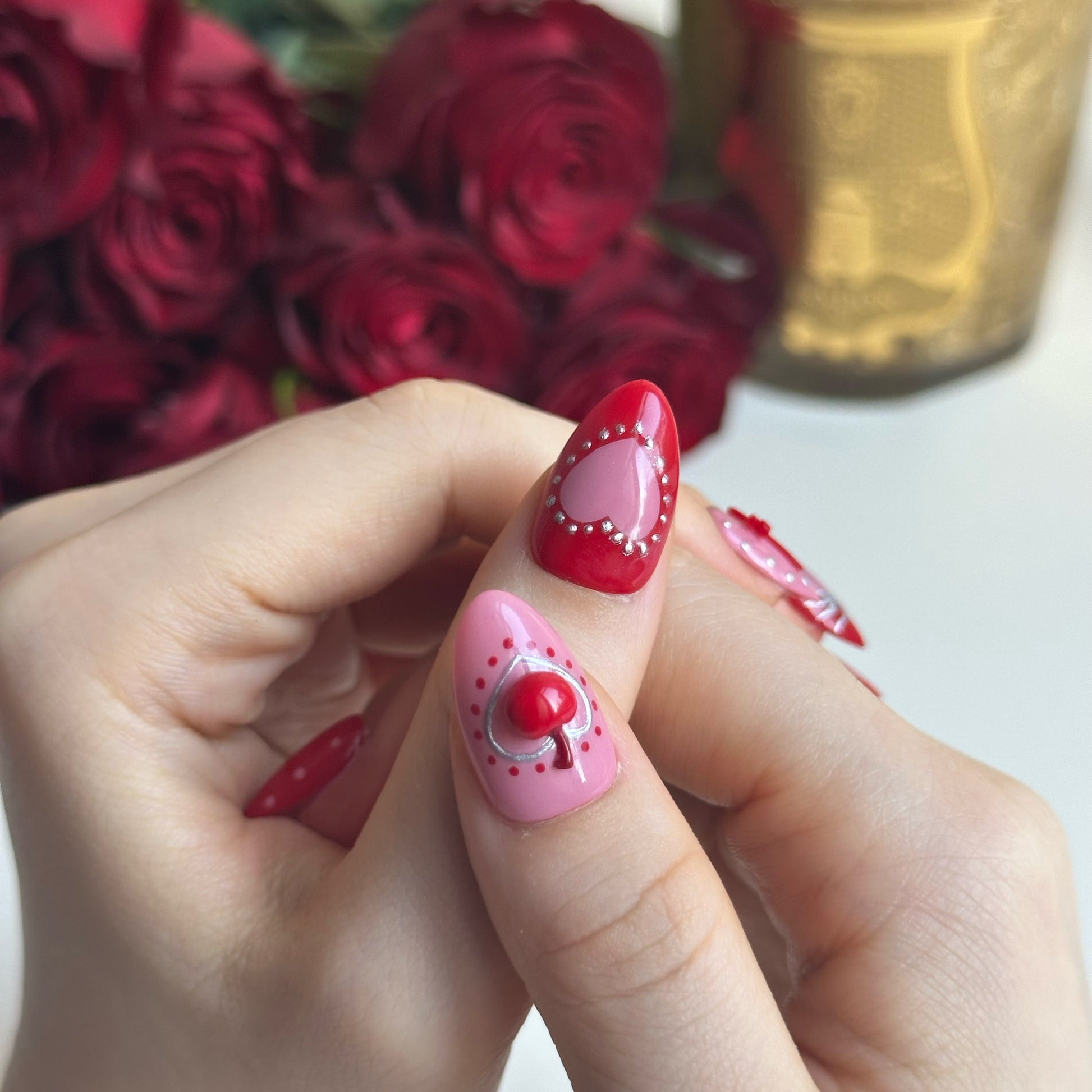 Silver Kisses is a reusable handmade press-on nails set by Leme. Elevate your Valentine's Day look with Silver Kisses, a high-quality short almond nail design from our exclusive Valentine's collection. This striking design features lustrous silver chrome accents paired with dimensional 3D cherry details, creating an eye-catching contrast. The bold palette of hot red and pink celebrates uninhibited romance and passionate self-expression. A glittering heart adorns the middle finger as the statement focal poin
