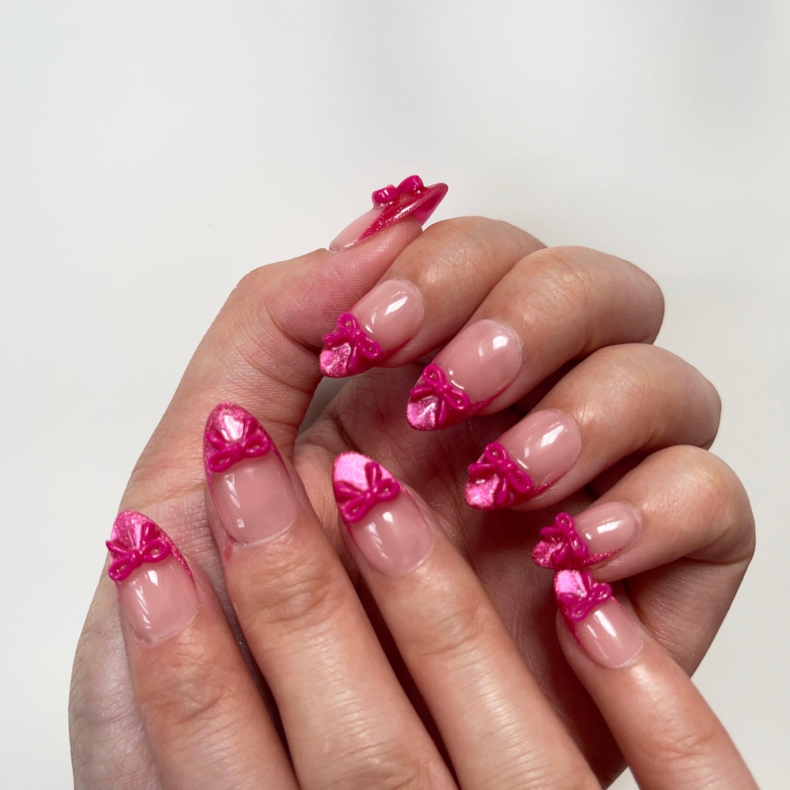 Sassy Diva is a reusable handmade press-on nails set by Leme. Elevate your manicure with the Sassy Diva nails, featuring a short almond shape and classic French tips enhanced by a vibrant hot pink cat-eye effect. Each nail is adorned with a delicate pink bow tie over a nude base, combining elegance with a playful edge. Crafted with high-quality materials, these nails offer durability and a flawless finish for a confident, expert look.