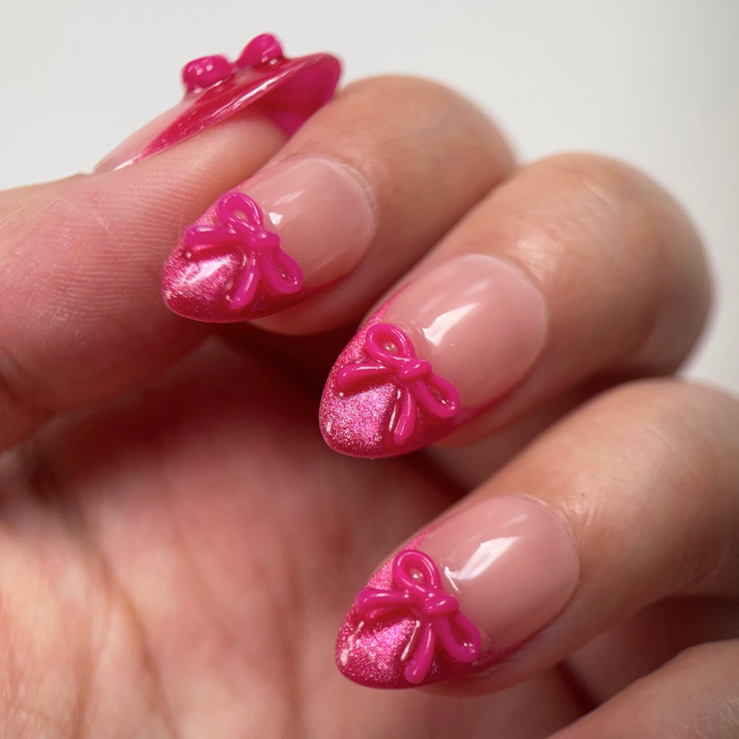 Sassy Diva is a reusable handmade press-on nails set by Leme. Elevate your manicure with the Sassy Diva nails, featuring a short almond shape and classic French tips enhanced by a vibrant hot pink cat-eye effect. Each nail is adorned with a delicate pink bow tie over a nude base, combining elegance with a playful edge. Crafted with high-quality materials, these nails offer durability and a flawless finish for a confident, expert look.