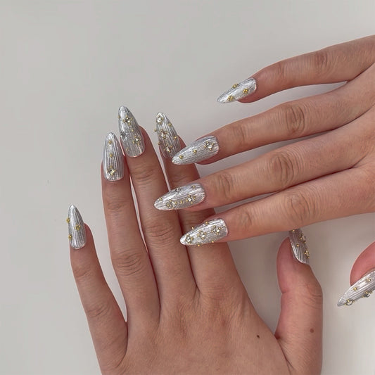 Siriver is a reusable handmade press-on nails set by Leme. Crafted with a medium almond shape, Siriver showcases a high-quality silver chrome finish inspired by the intricate Buccellati style. Adorned with delicate mini golden balls and clear pearls, this piece blends classic elegance with subtle opulence, perfect for those who appreciate expert craftsmanship and timeless design.