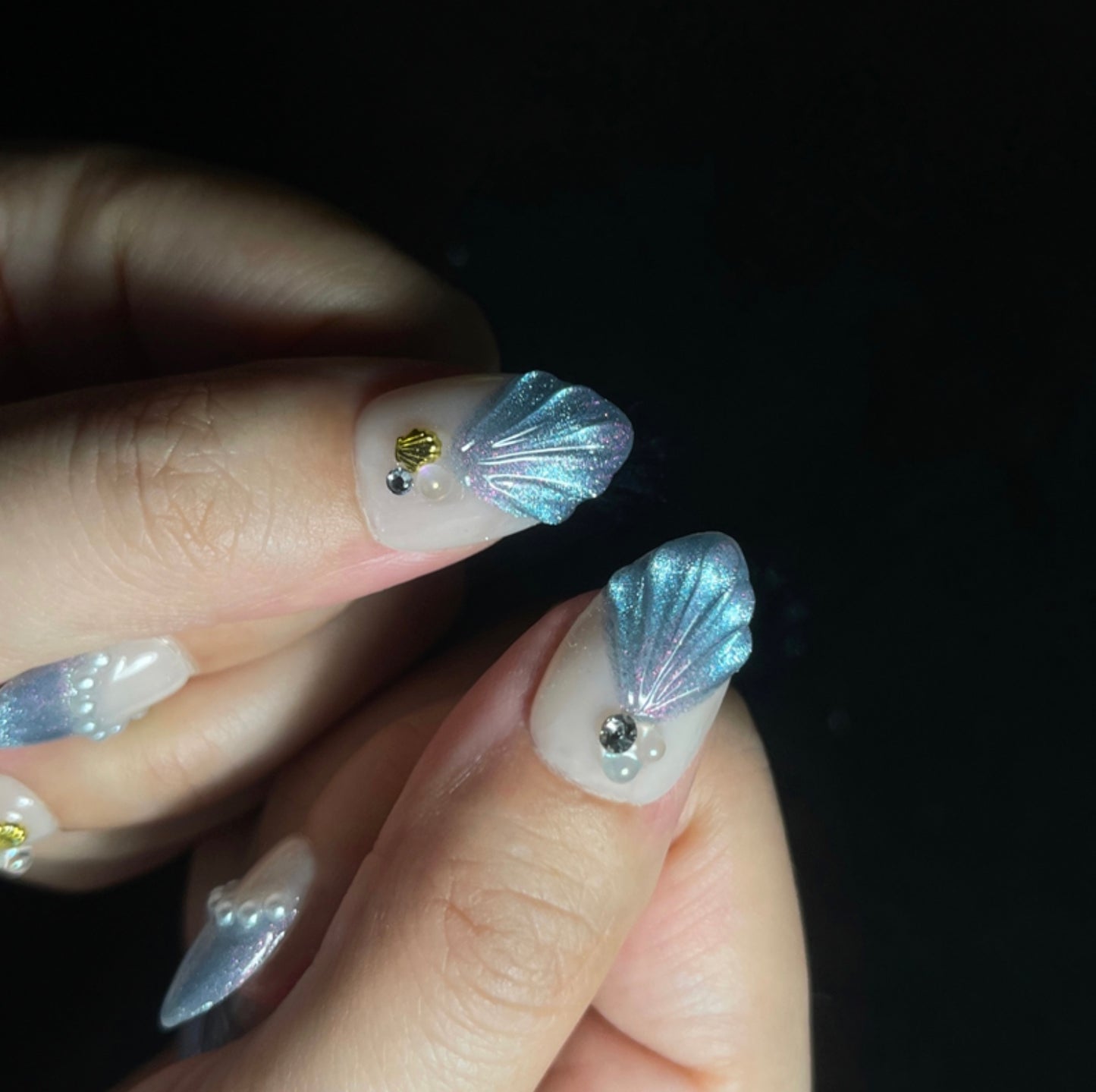 Treasure Beneath is a reusable handmade press-on nails set by Leme. Experience the elegance of "Treasure Beneath" nails, featuring expertly crafted short almond-shaped tips with a sophisticated blue cat-eye effect. These high-quality 3D nails showcase delicate water-inspired designs on a pristine white base, accented with lustrous pearls for a refined, dimensional look. Perfect for those seeking a subtle yet striking manicure that combines artistry with durability.