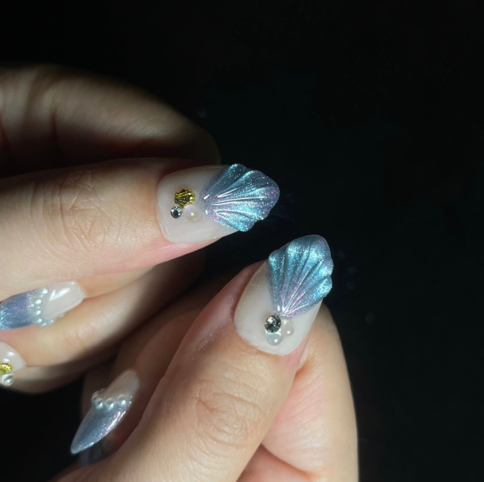 Treasure Beneath is a reusable handmade press-on nails set by Leme. Experience the elegance of "Treasure Beneath" nails, featuring expertly crafted short almond-shaped tips with a sophisticated blue cat-eye effect. These high-quality 3D nails showcase delicate water-inspired designs on a pristine white base, accented with lustrous pearls for a refined, dimensional look. Perfect for those seeking a subtle yet striking manicure that combines artistry with durability.