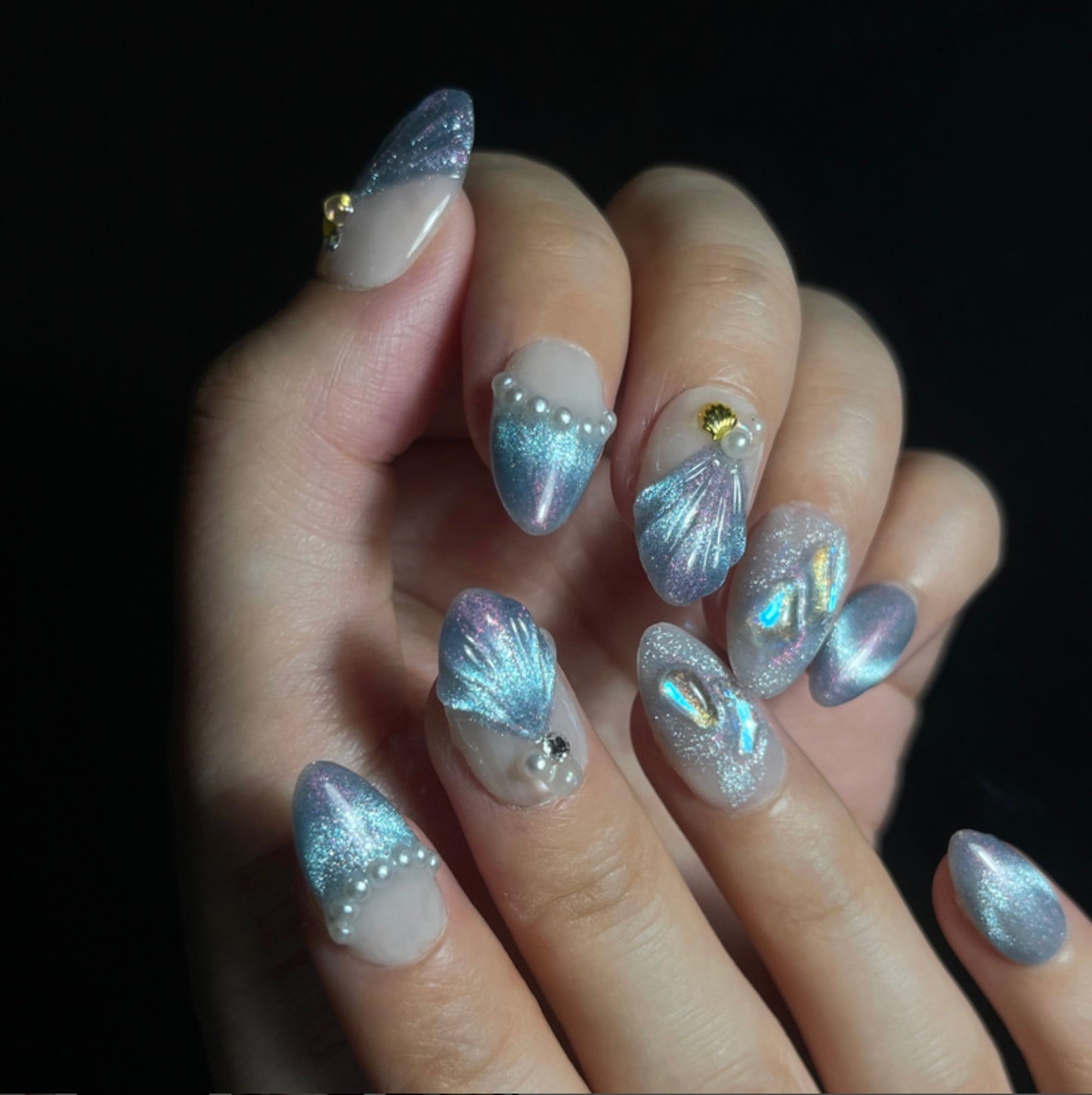 Treasure Beneath is a reusable handmade press-on nails set by Leme. Experience the elegance of "Treasure Beneath" nails, featuring expertly crafted short almond-shaped tips with a sophisticated blue cat-eye effect. These high-quality 3D nails showcase delicate water-inspired designs on a pristine white base, accented with lustrous pearls for a refined, dimensional look. Perfect for those seeking a subtle yet striking manicure that combines artistry with durability.