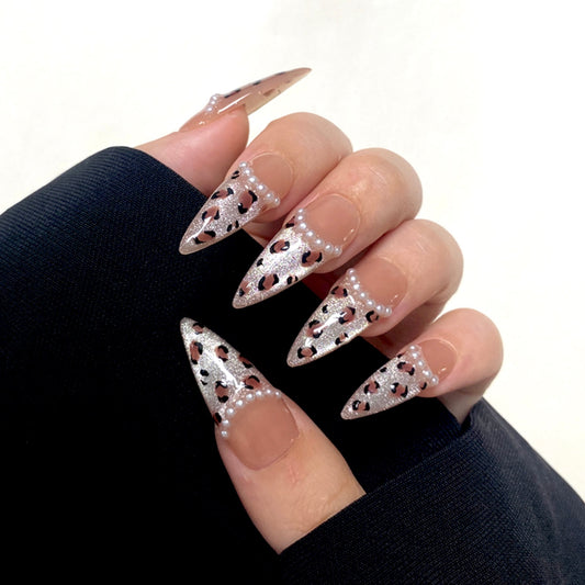 Wild Cat is a reusable handmade press-on nails set by Leme. Elevate your nail game with "Wild Cat," featuring expertly crafted long stiletto nails adorned with chic cat-eye French tips. This high-quality set combines elegant nude tones with striking leopard patterns and delicate pearl accents, delivering a sophisticated yet bold look perfect for those who appreciate refined artistry and daring style.